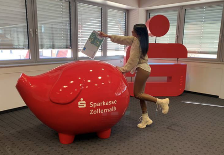 Junge Frau füttert rotes Sparschwein mit 100 Euroschein