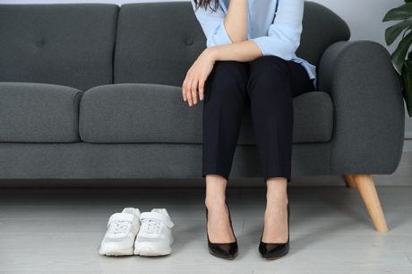 Frau sitzt auf Sofa, vor ihr stehen Pumps und Sneakers